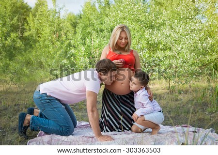 father and son kissing woman\'s pregnant belly outdoor