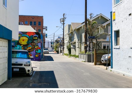 VENICE BEACH, USA - JUNE 4, 2014: A residential back road with a colorful mural painting in the background. On the roadside cars are parked. There are a redbrick house, wooden houses and stone houses.