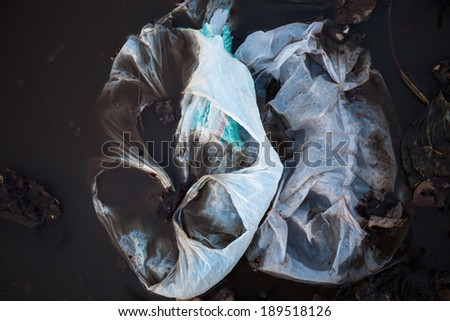 Thrown away plastic bags floating in black dirty water