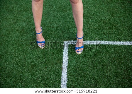 Woman legs in high heel sandals on the soccer field near the white line