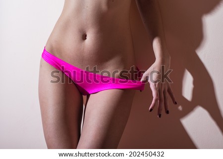 close up image of sexy glamor girl young woman having fun posing near wall showing her body fitness hips in pink lingerie on light copy space background