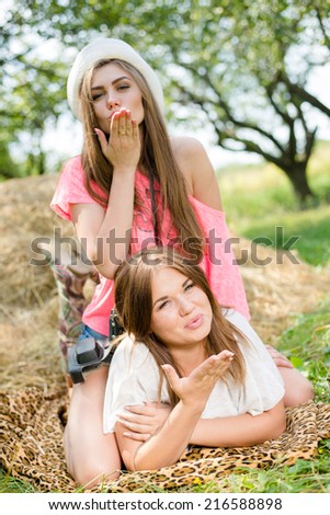 portrait of blowing kiss 2 pretty girls best friends having fun relaxing lying on hay happy smiling & looking at camera on green summer outdoors copy space background