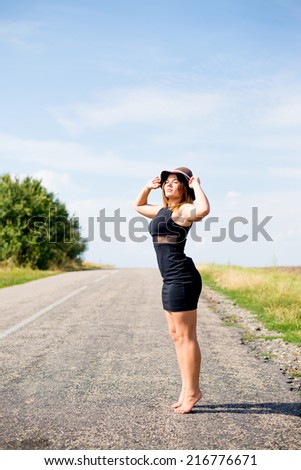 road adventure: elegant pretty girl on empty road looking up posing on summer blue sky copy space background