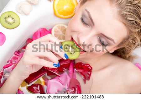 spa relaxation with fruits: closeup portrait of seductive sexy young woman lying relaxing in bath with rose petals and fruit slices, happy enjoying eyes closed