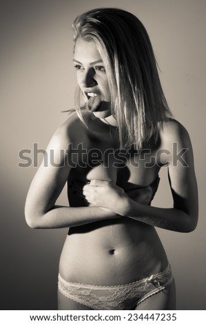 sexy tongue out: portrait of beautiful blond young woman posing hiding covered topless chest looking at copy space on light background & showing tongue