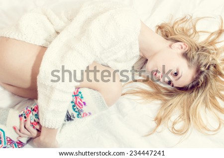 blue eyes beauty in bed: portrait of beautiful blond sexy young woman on white copy space background wearing just hand made jumper and knee socks