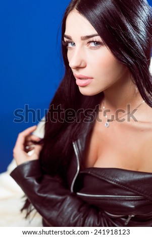 closeup portrait of hot sexy pretty young lady wearing leather jacket sensually looking at camera on blue copy space background