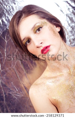 Closeup portrait of sexy beautiful young woman covered in shining make up on silver background