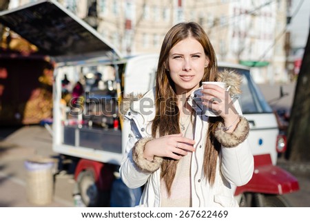 Portrait of young pretty woman with a cup of hot drink on sunny outdoors background