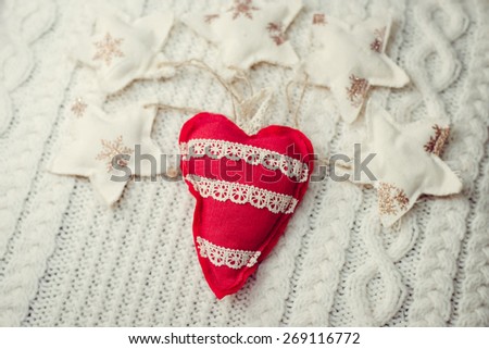 Closeup picture of handmade red heart on knitted background surrounded with decorative stars
