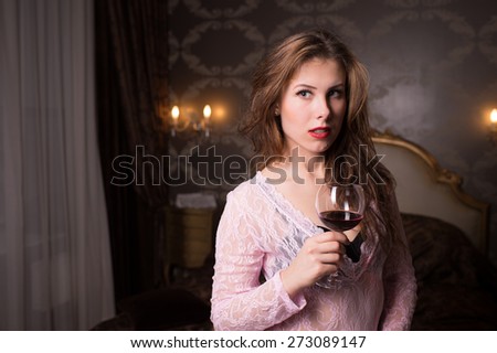 Portrait of beautiful young lady with a glass of wine on luxury bedroom background
