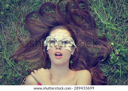 closeup portrait of sensual beautiful brunette young lady having fun wearing mask relaxing lying on green grass copy space background