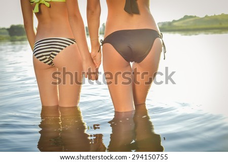 Closeup picture on 2 beautiful young women with perfect fitness shape buttocks having fun posing on summer water outdoors copy space background