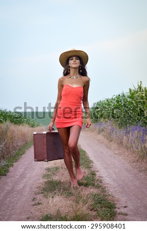 Portrait of beautiful young lady holding suitcase in hand and walking on sunny day outdoors landscape