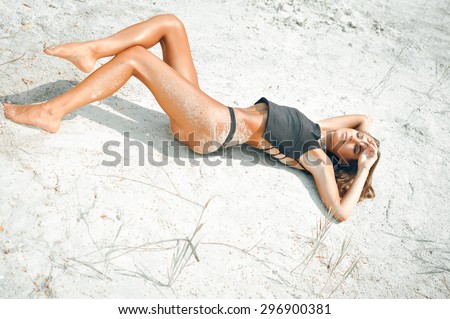 Portrait of beautiful sexy young lady laying on the sand ground on sunshine outdoors background