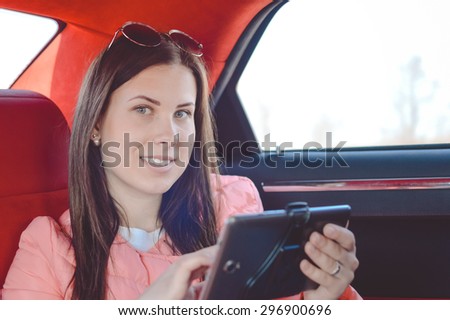 Portrait of beautiful young woman busy on the mobile tablet in luxury car