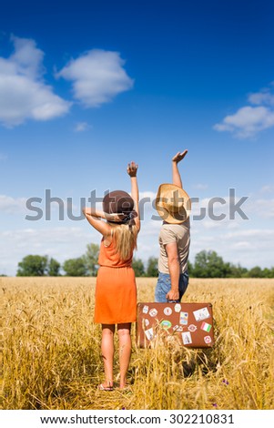 Picture of holding hands up and waving together beautiful couple with travel suitcase on the field outdoors background