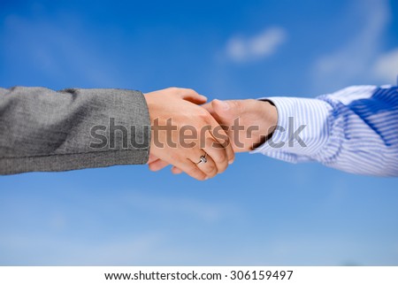 Business people handshaking on blue sky sunny outdoors background, close-up picture
