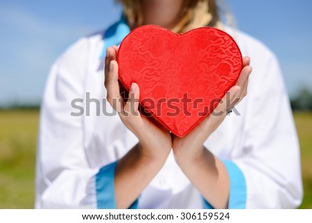 Close up of doctor holding hands with heart on sunny outdoors background