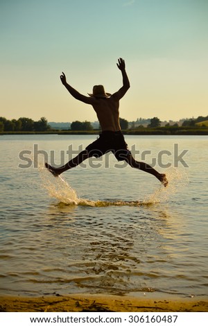 Silhouette of person running or jumping for fun above the water on the beach summer outdoors background