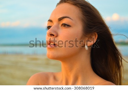 Close up picture of young brunette sensual  pensive lady on beach by sea at sunset