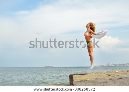 Young lady with arms extended sidewards jumping up on rocky beach by sea exposing her perfect body to sun copyspace on summer day outdoors background