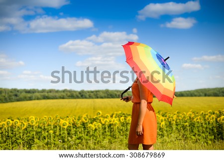 Picture of female in orange dress under colorful umbrella standing in field of sunflowers on sunny day outdoors background