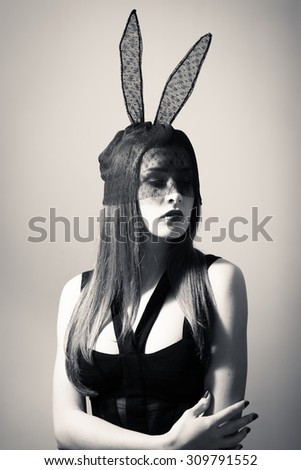 black and white photography portrait of sexy pretty girl wearing black dress and lace bunny ears. Young woman looking down.
