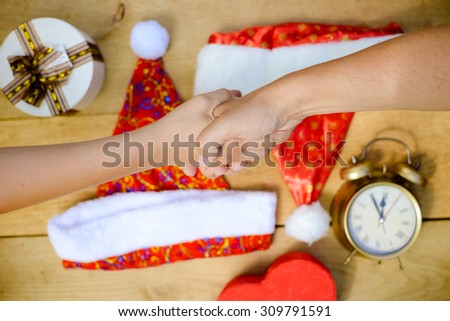 Shaking hands above desk with Christmas hats, clock and giftbox. Organize and coordinate plans to be in time with Christmas present for everybody.