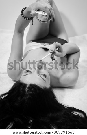 Black and white portrait of beautiful gorgeous young brunette lady having fun drawing lipstick relaxing lying in lingerie on white bed