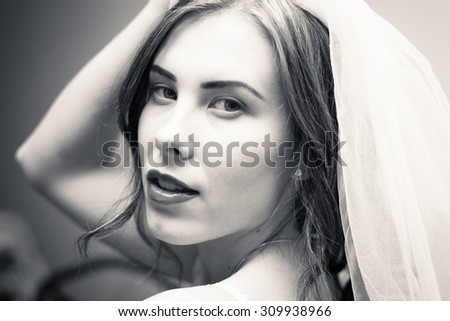 Closeup portrait of young bride in white veil with open mouth and raised hand. Photo in black and white.