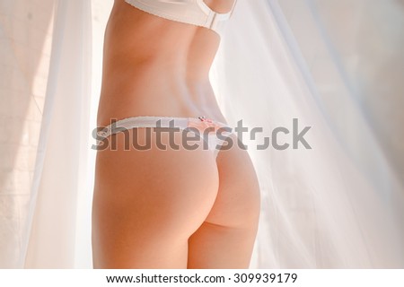 Closeup of women half length body back in white strings. Blurred background with white curtain.