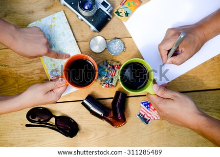 Close-up picture of two persons hands working in team at wooden table. The following objects are used on the table for work: map, papers, film camera, coffee, compass, etc.