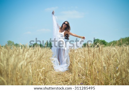 Beautiful glamour girl dancing in the wheat field and breathing deep fresh air. Long haired woman in sunglasses posing for photographer with white cloth.