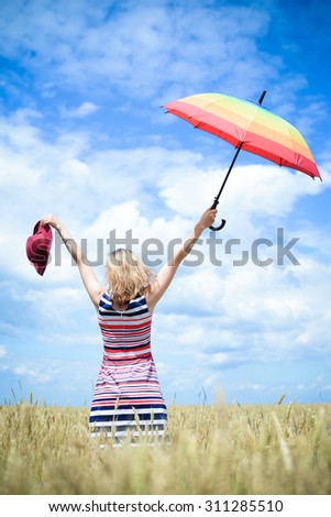 Happy dreamer enjoying her life with raised hands to the clouds. Lady posing with umbrella in the right and hat in the left hands.