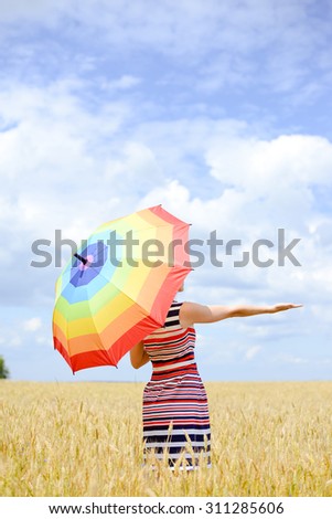 Happy lady hiding from the burning sun behind the multi-coloured rainbow umbrella in stripped summer dress offering hand.