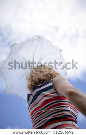 Blond female under umbrella looking up at cloud sky. Woman in striped dress rising white umbrella