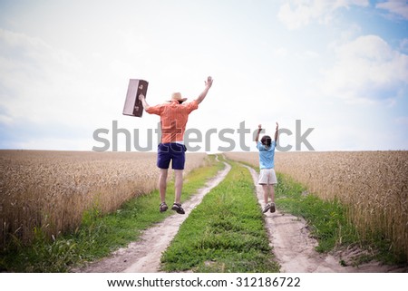 Father and son jumping on road between field of wheat background. Backview of man with old valize and little boy over blue sky Imagine de stoc © 
