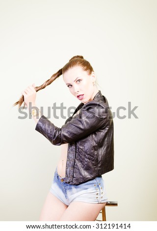 Sexy pretty girl wearing black leather jacket and denim shirts sitting on chair. Half length of model on light background.