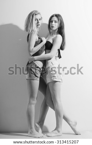 Black and white photography of two fashion sexy romantic beautiful girls in jeans shorts having fun and good time hugging each other. portrait on light copy space background