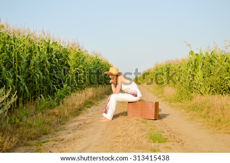 Picture of woman wearing straw hat sitting on suitcase in country. Sideview of young girl resting on blue sky sunny outdoors background. Imagine de stoc © 