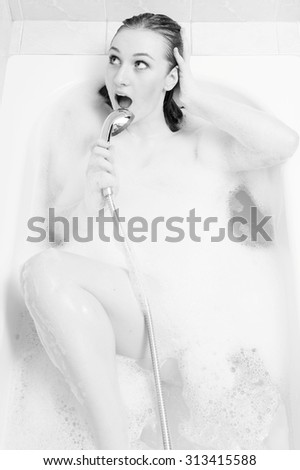 Picture of excited beautiful sexy lady singing in luxury spa bath using shower handle. Black and white photography