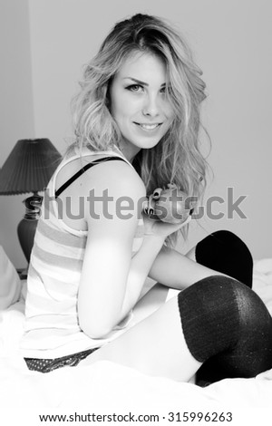 Portrait of sexi blonde beautiful girl in lingerie having fun happy smiling holding big apple sitting on bed on light copy space background. Black and white photography