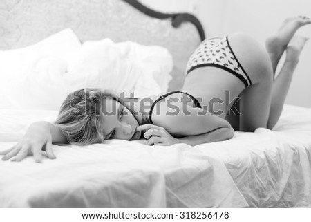 Black and white photography of beautiful blond sexy young lady on bed with buttocks up on light background. Picture closeup.