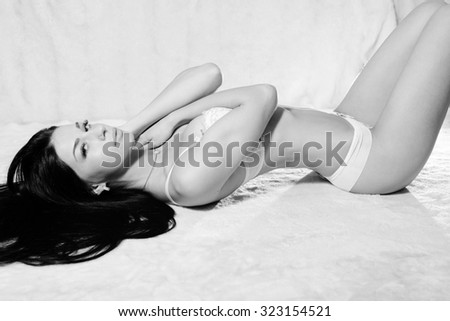 Black and white photography portrait of amazing sexy beautiful young lady in great shape with long luxury hair relaxing on light copy space background.
