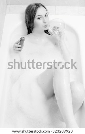 Black and white portrait of gorgeous young sensual woman having fun blowing soap bubble. Sexy girl happy smiling relaxing and enjoying laying in spa bath on foam water background