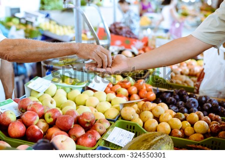 Picture of marketplace with different fruits. Buyer\'s hand and seller\'s hand on blurred colorful background.