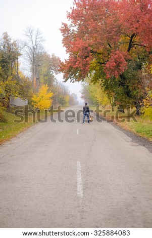 Picture of beautiful young woman with guitar standing on countryside road. Backview of pretty girl in black jacket and jeans on autumn foggy outdoor background.