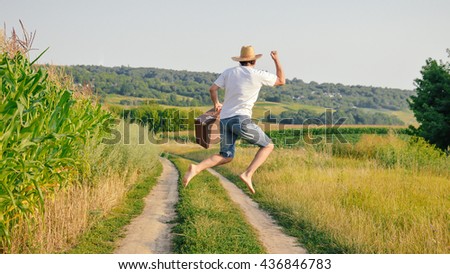 Back view of man in hat with old suitcase on wheat field. Excited traveler on summer sunny countryside background. Imagine de stoc © 