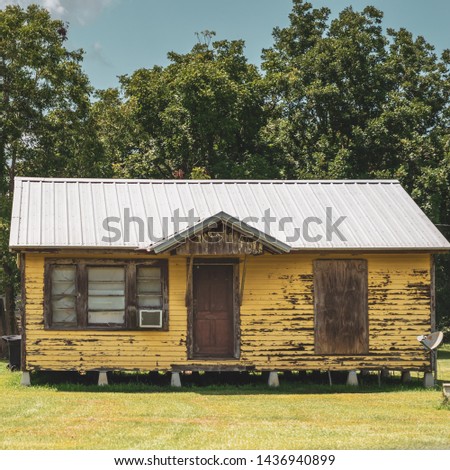 A Cajun style cottage home made of wood with yellow paint that is chipped and falling off the wood, sitting on cement pillars located in a flood zone, once hurricane damaged in South Louisiana. Imagine de stoc © 